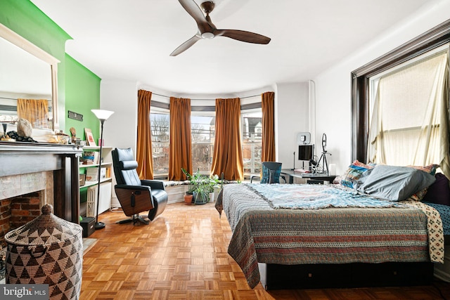 bedroom with ceiling fan, a brick fireplace, and light parquet floors