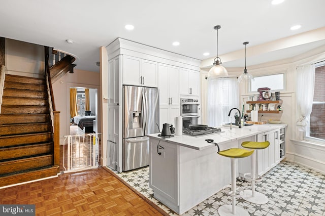 kitchen with white cabinetry, hanging light fixtures, stainless steel appliances, a kitchen breakfast bar, and light stone counters