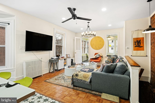 living room with parquet floors, radiator heating unit, and ceiling fan with notable chandelier