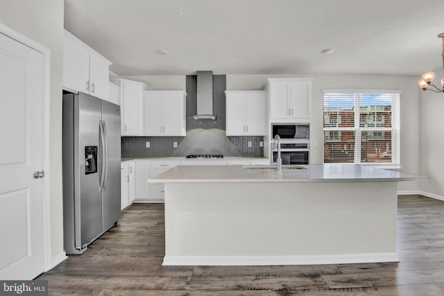 kitchen with white cabinets, appliances with stainless steel finishes, a kitchen island with sink, and wall chimney range hood