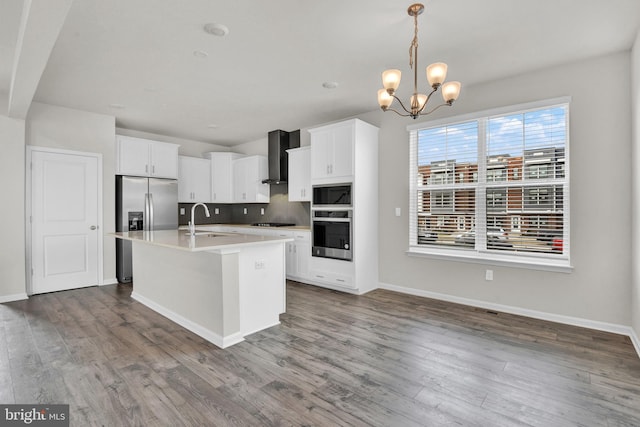 kitchen featuring pendant lighting, sink, a kitchen island with sink, stainless steel appliances, and wall chimney exhaust hood