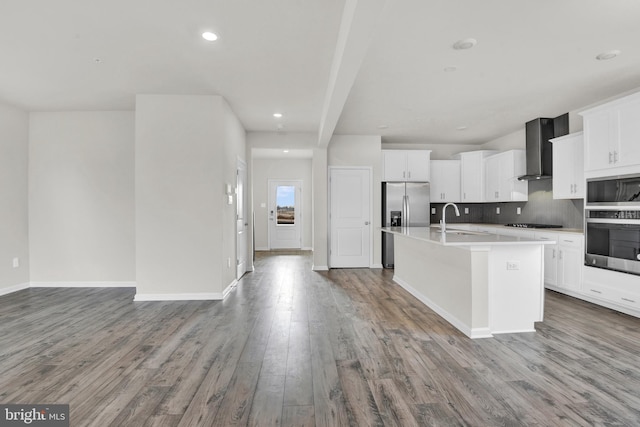 kitchen featuring wall chimney exhaust hood, appliances with stainless steel finishes, a center island with sink, and white cabinets