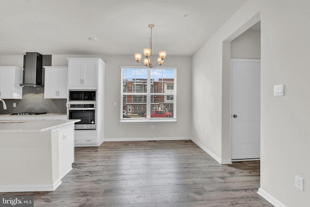 kitchen featuring wall chimney range hood, stainless steel appliances, tasteful backsplash, wood-type flooring, and white cabinets