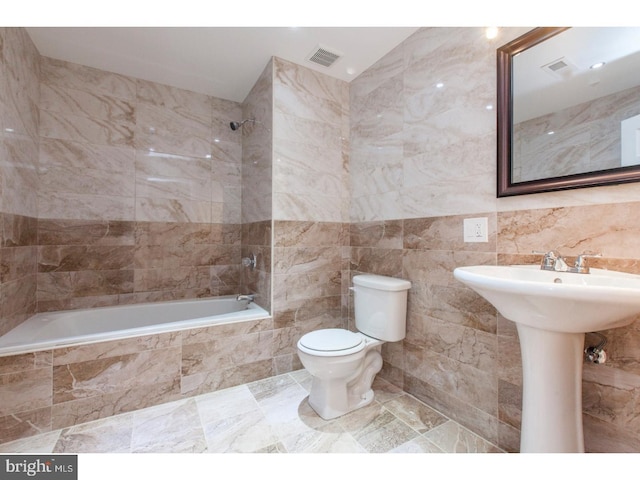 full bathroom featuring tiled shower / bath, sink, tile walls, and toilet