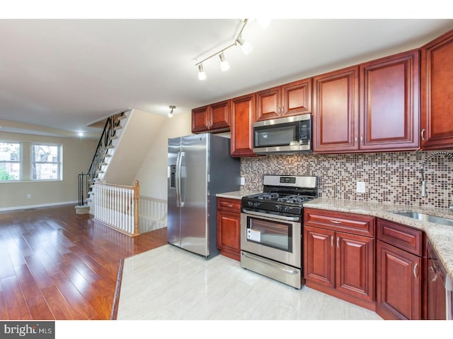 kitchen with stainless steel appliances, light stone countertops, sink, and backsplash