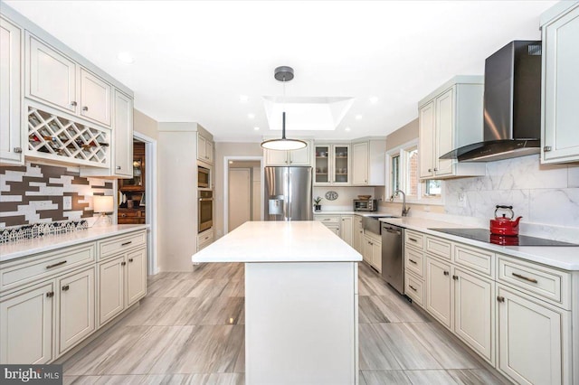 kitchen featuring light countertops, appliances with stainless steel finishes, a kitchen island, wall chimney range hood, and a sink