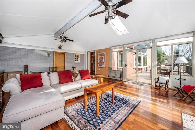 living room featuring a ceiling fan, vaulted ceiling with skylight, brick wall, and wood finished floors