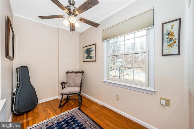 living area featuring a ceiling fan, crown molding, baseboards, and wood finished floors