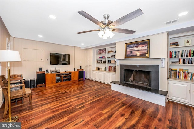 living area with built in shelves, a fireplace, visible vents, ceiling fan, and wood finished floors