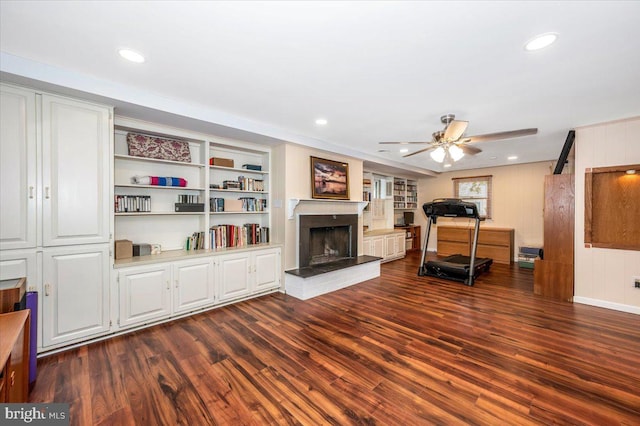 exercise room with a fireplace with raised hearth, ceiling fan, built in shelves, recessed lighting, and wood finished floors