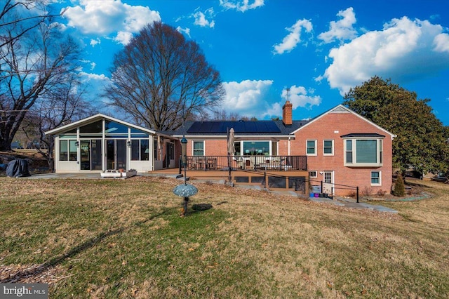 rear view of property featuring brick siding, a sunroom, a yard, roof mounted solar panels, and a chimney