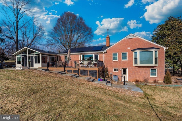 rear view of house with a patio, brick siding, a sunroom, roof mounted solar panels, and a chimney