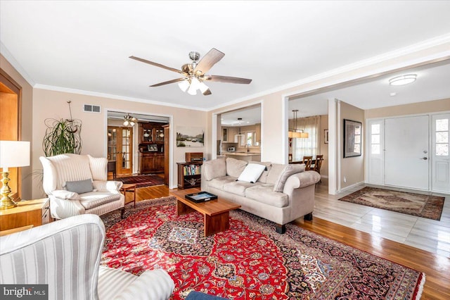 living area with baseboards, crown molding, visible vents, and wood finished floors