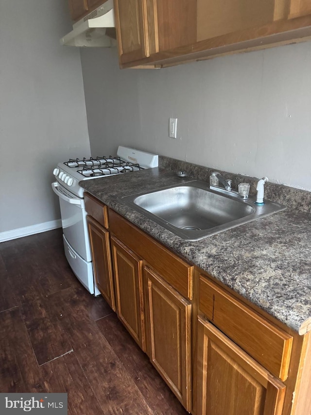 kitchen featuring sink, dark wood-type flooring, gas range gas stove, and dark stone counters