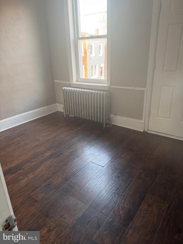 spare room featuring dark wood-type flooring and radiator heating unit