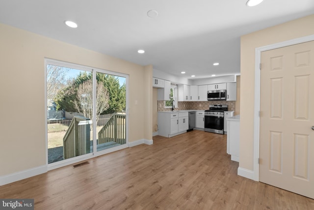 kitchen with sink, white cabinets, decorative backsplash, stainless steel appliances, and light wood-type flooring