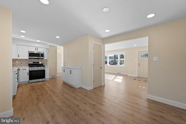 kitchen featuring white cabinetry, stainless steel appliances, light hardwood / wood-style floors, and decorative backsplash