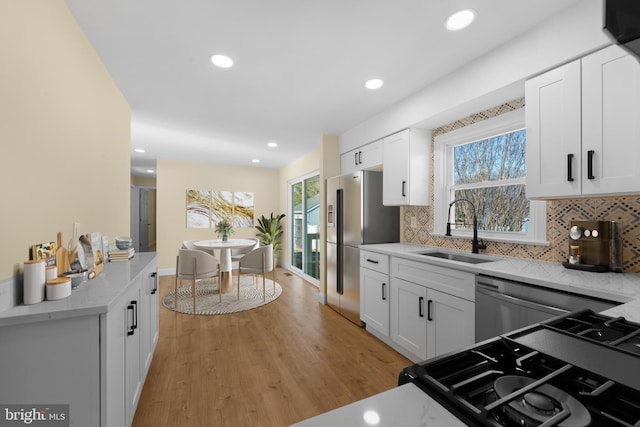 kitchen with sink, white cabinets, light hardwood / wood-style floors, stainless steel refrigerator with ice dispenser, and light stone countertops