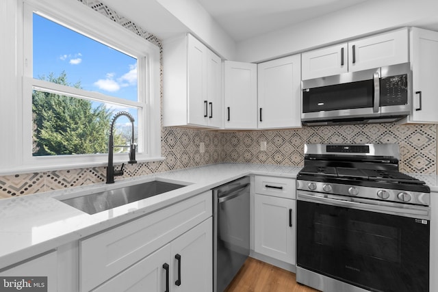 kitchen with sink, light stone counters, stainless steel appliances, decorative backsplash, and white cabinets