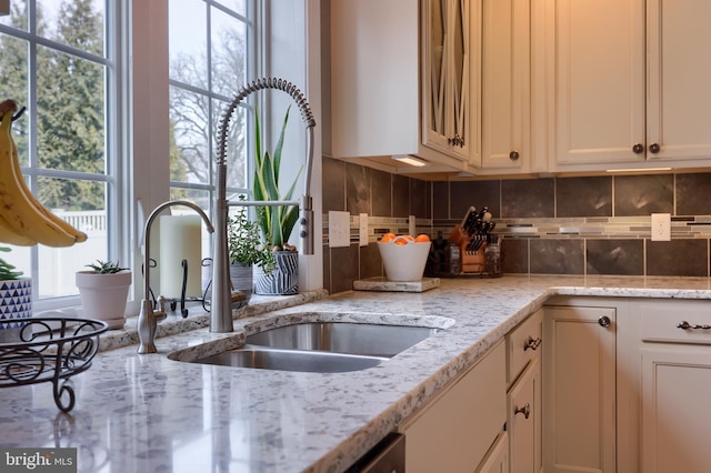 kitchen featuring white cabinets, light stone countertops, sink, and backsplash