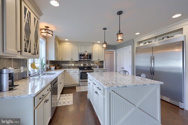 kitchen with sink, stainless steel appliances, a center island, light stone countertops, and decorative light fixtures