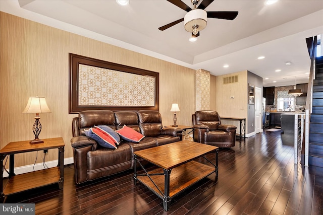 living room with a raised ceiling, dark wood-type flooring, and ceiling fan