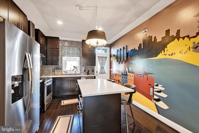 kitchen featuring dark hardwood / wood-style floors, decorative light fixtures, a breakfast bar area, a center island, and stainless steel appliances