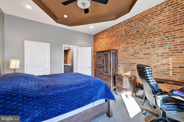 carpeted bedroom with a tray ceiling, ceiling fan, and brick wall