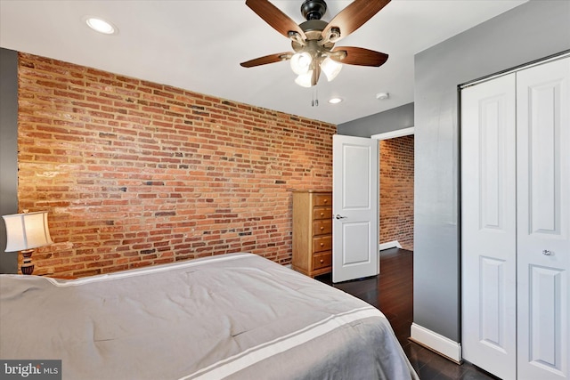 bedroom with brick wall, dark wood-type flooring, ceiling fan, and a closet