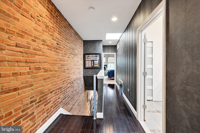 corridor with wood-type flooring and brick wall