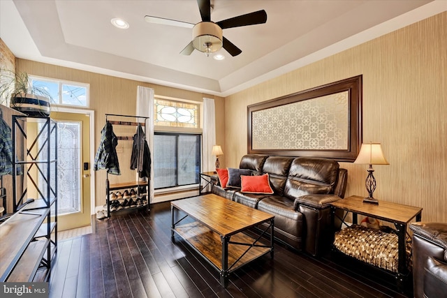 living room with a tray ceiling, dark wood-type flooring, and ceiling fan