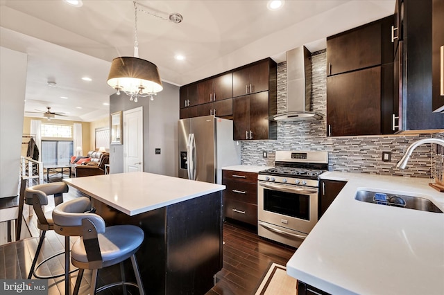 kitchen with wall chimney range hood, sink, dark wood-type flooring, a breakfast bar, and stainless steel appliances