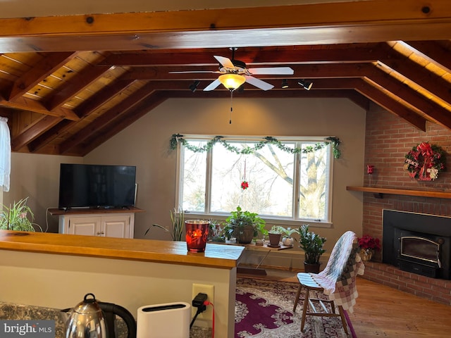 living room featuring a brick fireplace, lofted ceiling with beams, ceiling fan, and light wood-type flooring