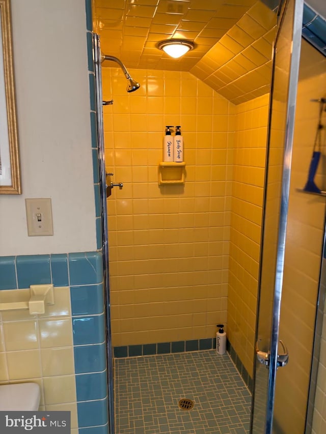 bathroom featuring walk in shower, toilet, and tile walls