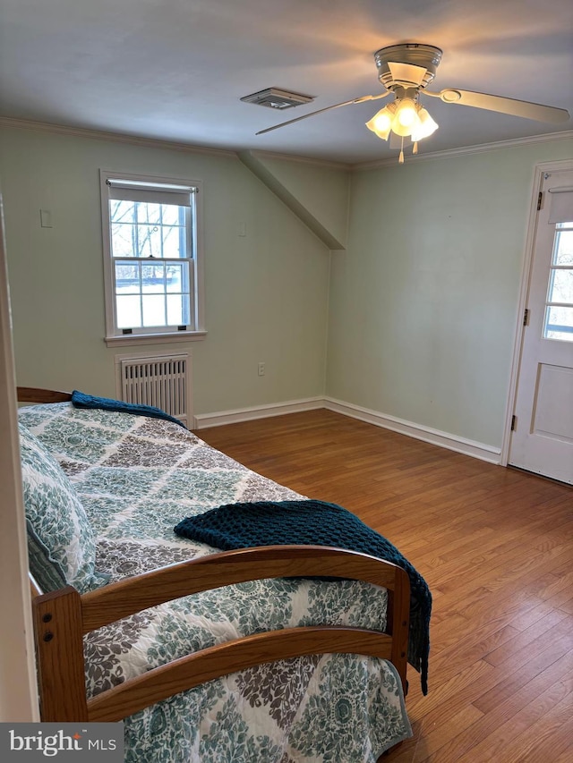 bedroom with wood-type flooring, radiator heating unit, ceiling fan, and crown molding