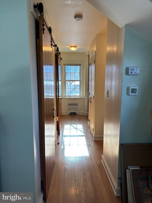 hallway featuring a barn door, radiator, and light hardwood / wood-style floors