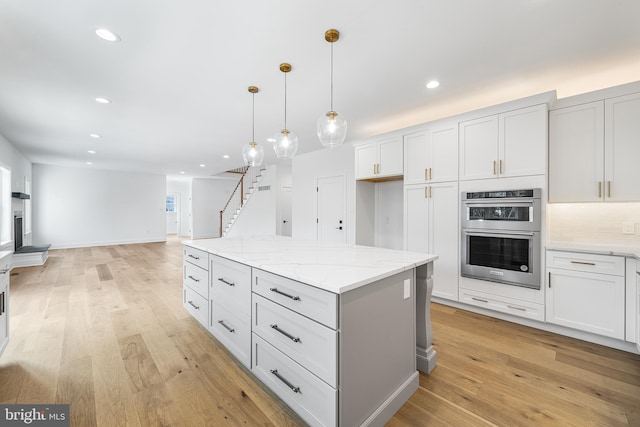 kitchen featuring hanging light fixtures, light stone countertops, white cabinets, and stainless steel double oven