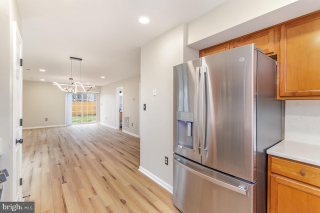 kitchen featuring stainless steel refrigerator with ice dispenser, pendant lighting, a notable chandelier, and light hardwood / wood-style floors