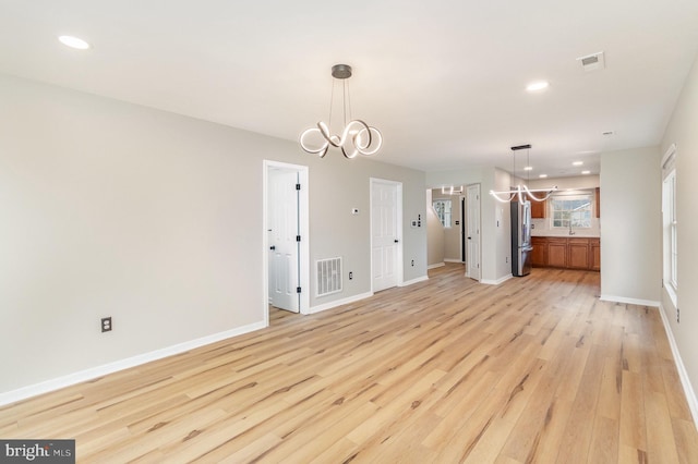 unfurnished living room with a chandelier, sink, and light wood-type flooring