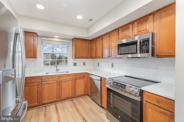 kitchen with stainless steel appliances, sink, backsplash, and light hardwood / wood-style floors