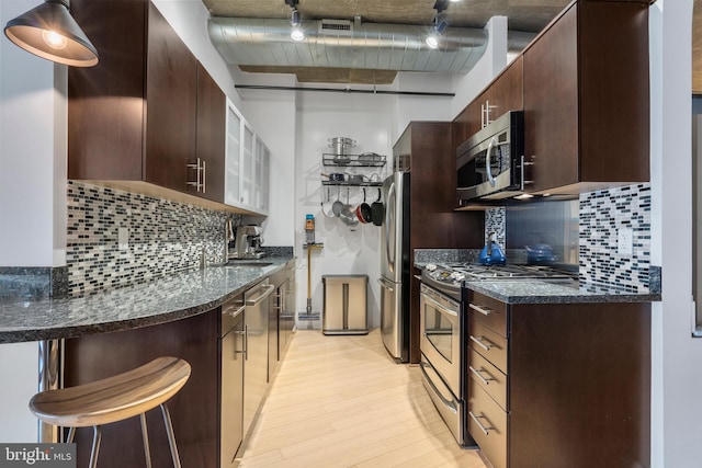 kitchen featuring appliances with stainless steel finishes, a kitchen breakfast bar, light hardwood / wood-style flooring, and dark stone countertops