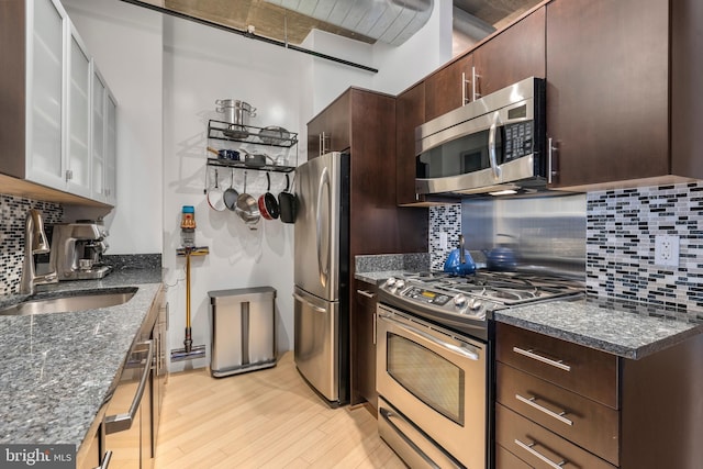 kitchen featuring sink, dark stone countertops, decorative backsplash, light hardwood / wood-style floors, and stainless steel appliances