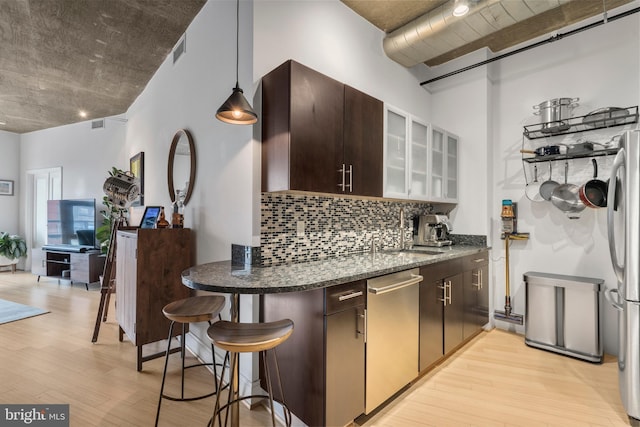 kitchen with hanging light fixtures, dark brown cabinets, light wood-type flooring, stainless steel appliances, and decorative backsplash