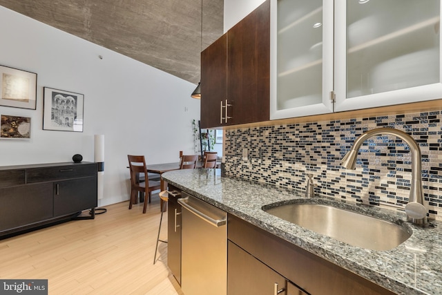 kitchen featuring dark brown cabinetry, sink, light hardwood / wood-style flooring, dark stone countertops, and dishwasher