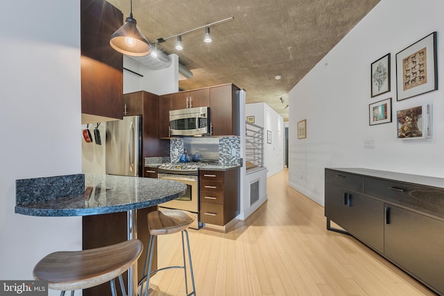 kitchen with appliances with stainless steel finishes, dark brown cabinetry, light hardwood / wood-style floors, a kitchen bar, and decorative light fixtures