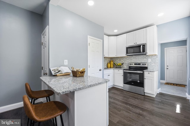 kitchen with appliances with stainless steel finishes, a breakfast bar, tasteful backsplash, white cabinetry, and light stone countertops