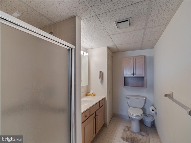 bathroom featuring a paneled ceiling, tile patterned flooring, vanity, toilet, and walk in shower