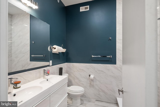 full bath featuring double vanity, a sink, toilet, and tile walls