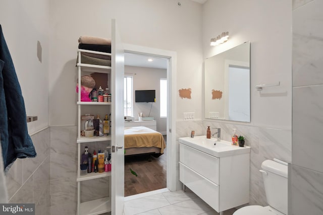 ensuite bathroom with tile walls, toilet, wainscoting, vanity, and ensuite bath