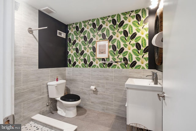 bathroom with wallpapered walls, visible vents, toilet, vanity, and tile walls